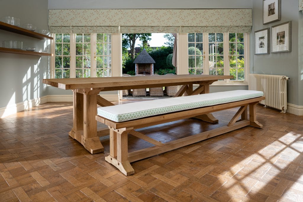 A large wooden dining table with cushioned bench seating in a dining room upon a wooden parqueted flooring