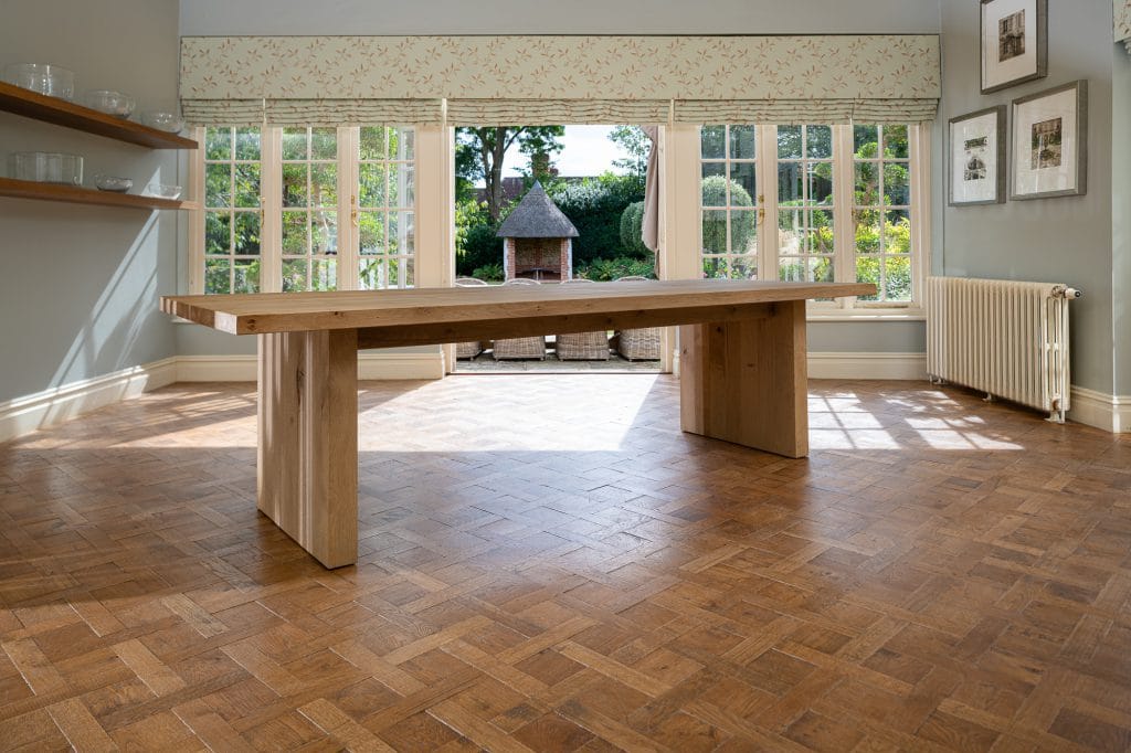 A wooden dining table in a dining room upon a wooden parqueted flooring