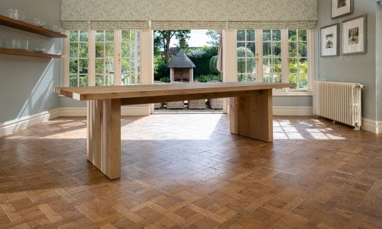 A wooden dining table in a dining room upon a wooden parqueted flooring