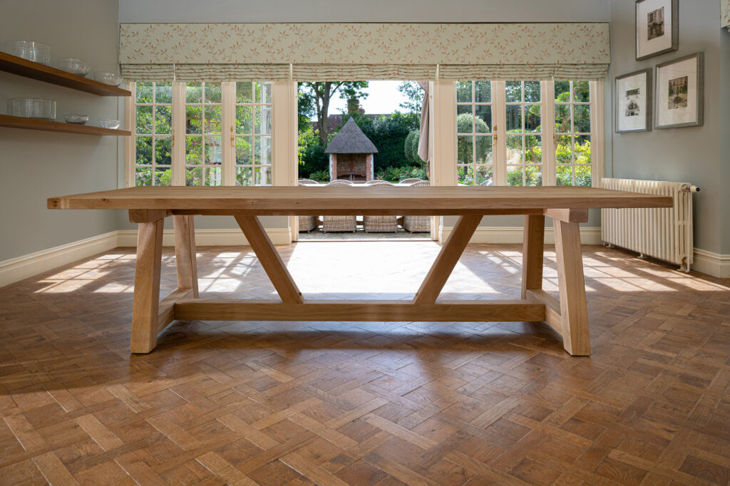 Oxenwood's wooden hollom large format dining table shown in a parquet floored dining room