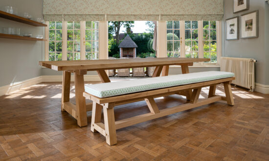 Oxenwood's wooden hollom large format dining table with cushioned benches shown in a parquet floored dining room