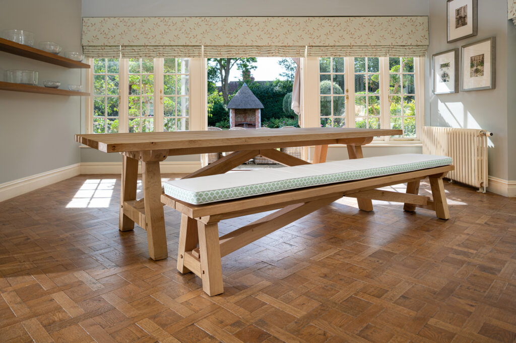 Oxenwood's wooden lucius large format dining table with cushioned benches shown in a parquet floored dining room