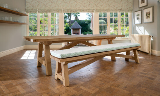 Oxenwood's wooden lucius large format dining table with cushioned benches shown in a parquet floored dining room