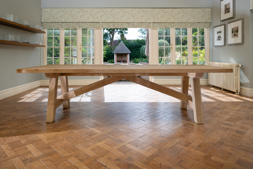 Oxenwood's wooden lucius large format dining table shown in a parquet floored dining room