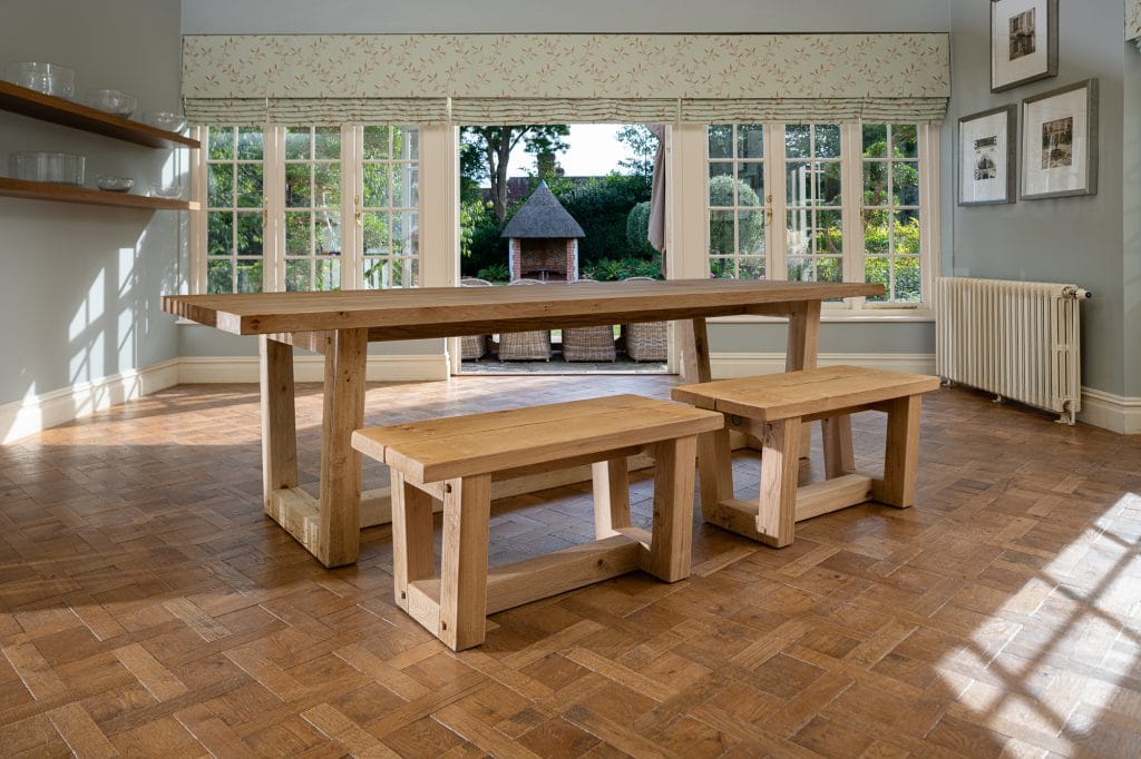 A wooden dining table and bench seating in a dining room upon a wooden parqueted flooring