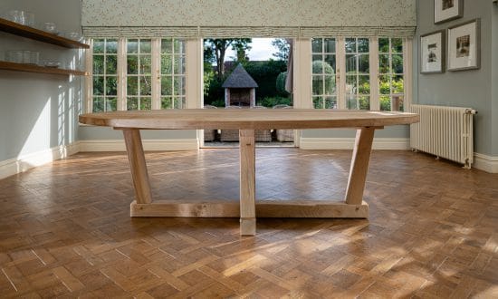 An oval wooden dining table in a dining room upon a wooden parqueted flooring