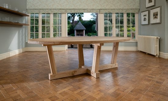 An oval wooden dining table in a dining room upon a wooden parqueted flooring