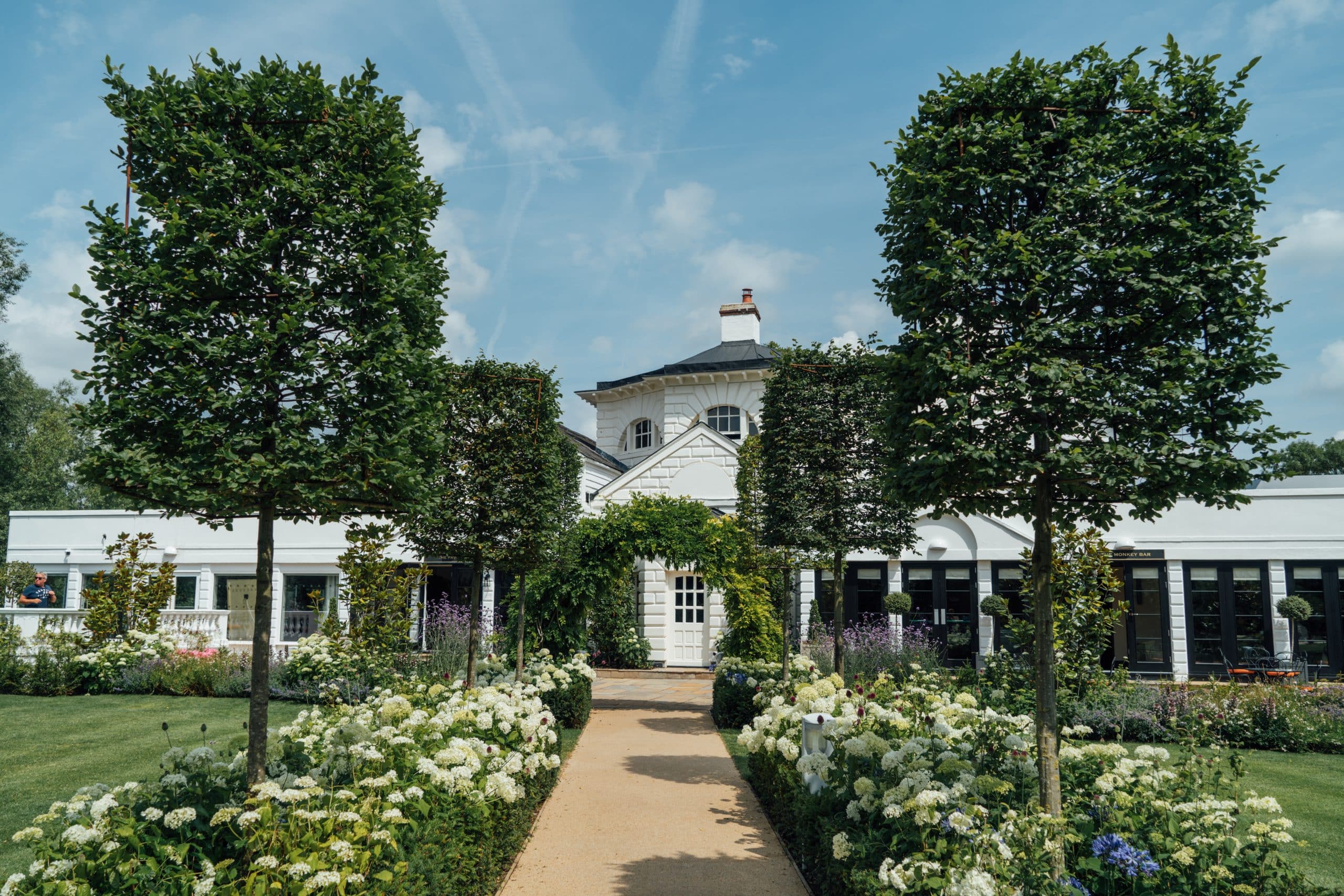 A garden, littered with white hydrageas and purple flowers in front of a white house