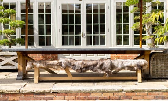 Oxenwood's Reindeer Hide Blankets on a wooden bench under a large outdoor dining table on a patio
