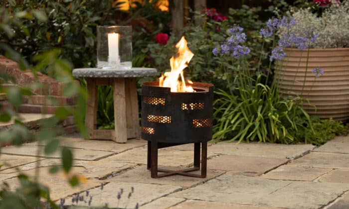 Oxenwood's Outdoor Fire Basket alight with blazing flames placed on a paved garden patio