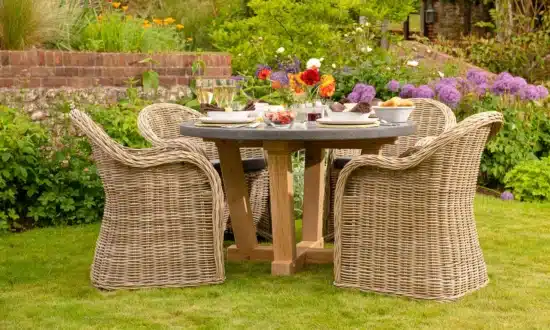 Oxenwood's circular outdoor dining table surrounded by woven dining chairs on a grassy garden area
