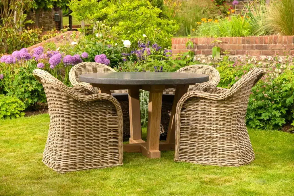 Oxenwood's circular outdoor dining table surrounded by woven dining chairs on a grassy garden area