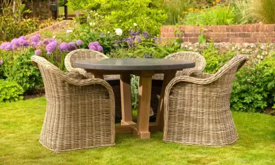 Oxenwood's circular outdoor dining table surrounded by woven dining chairs on a grassy garden area