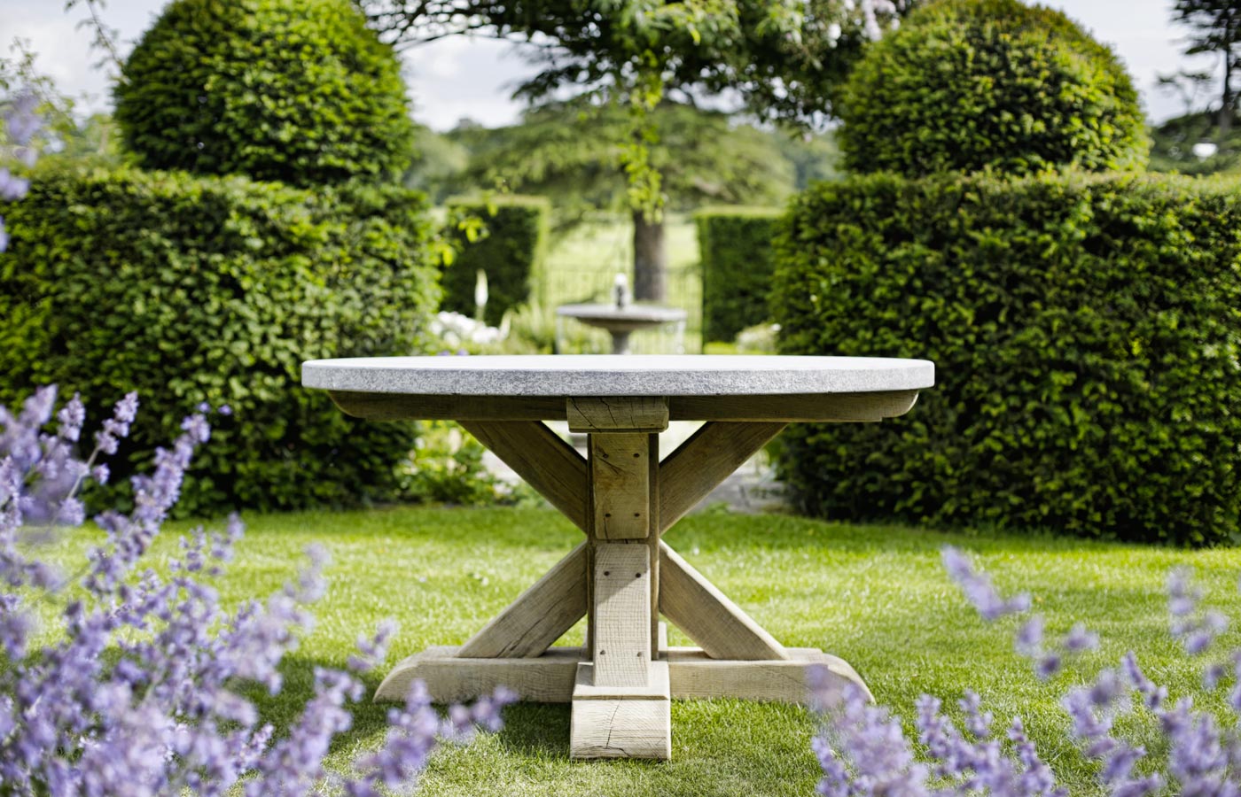 Jonas round outdoor dining table with bluestone top and wooden legs, set in a grassy garden area